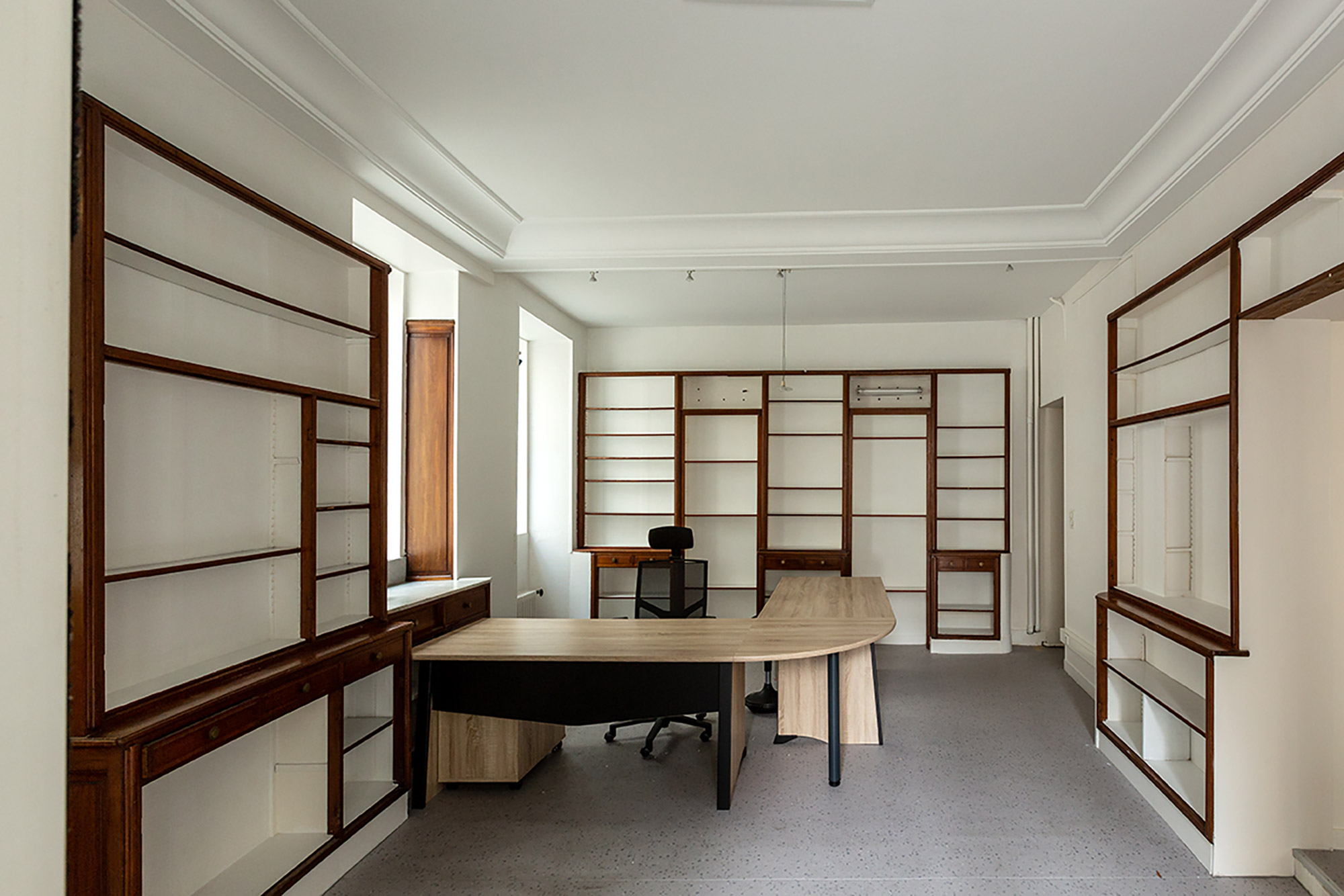 LP-home-Bibliothèque-vide-marron-before Bureau vide avant aménagements, avec bibliothèques murales en bois, grands rangements blancs, espace pour bureau et table de réunion ovale.